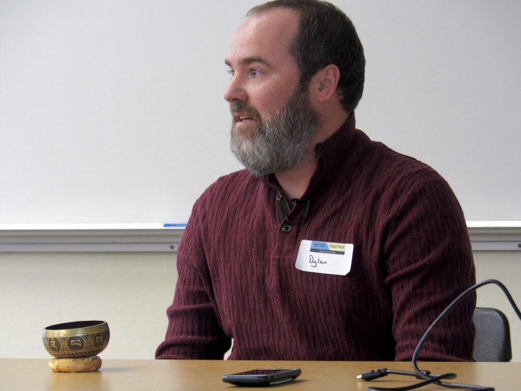 A photo of Dylan LeRoy at the Better Together Conference in 2022. He is sitting at a desk with a metal bowl placed on the desk in front of him,