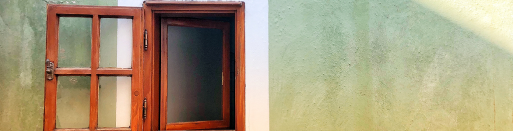 An outside wall of a house with a wooden window shutter wide open and a frosted glass window partially open